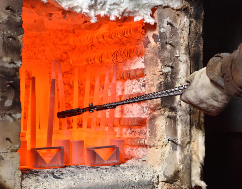 Worker pulls out the heated parts with tongs from an electric furnace for hardening metal. Dangerous work with high temperatures in heavy industry in a valve manufacturing plant